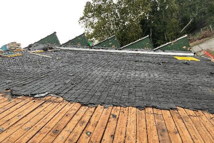 An unfinished roof with exposed wooden slats on the lower half and a dark, weathered underlayment on the upper section.
