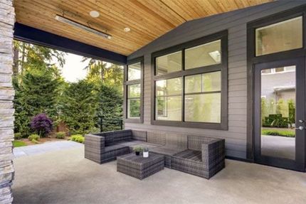 A flat roof with several HVAC units and ventilation fans against a backdrop of trees and a bright blue sky.
