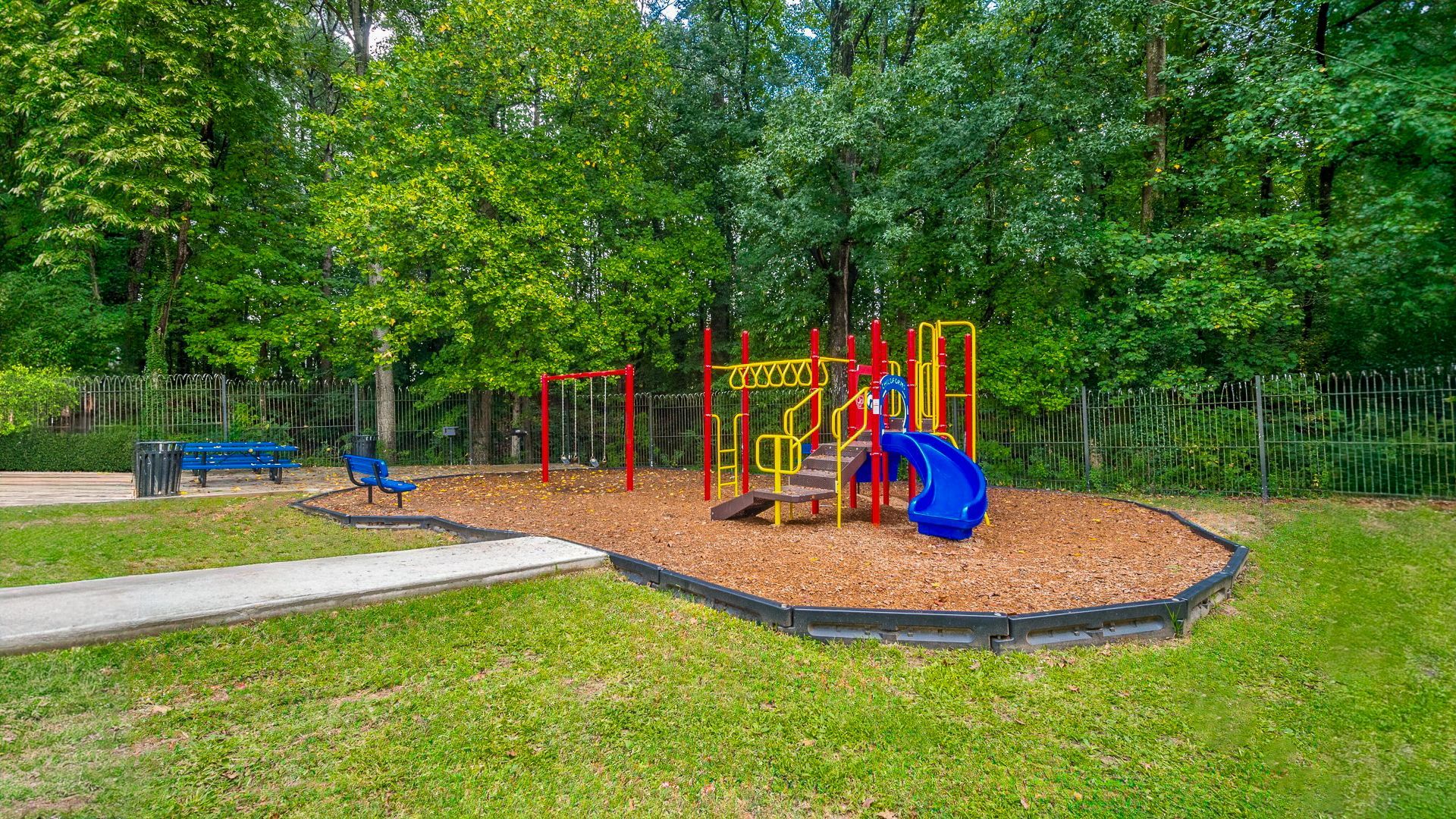 Colorful playground with slides and climbing structures in a park, surrounded by trees.