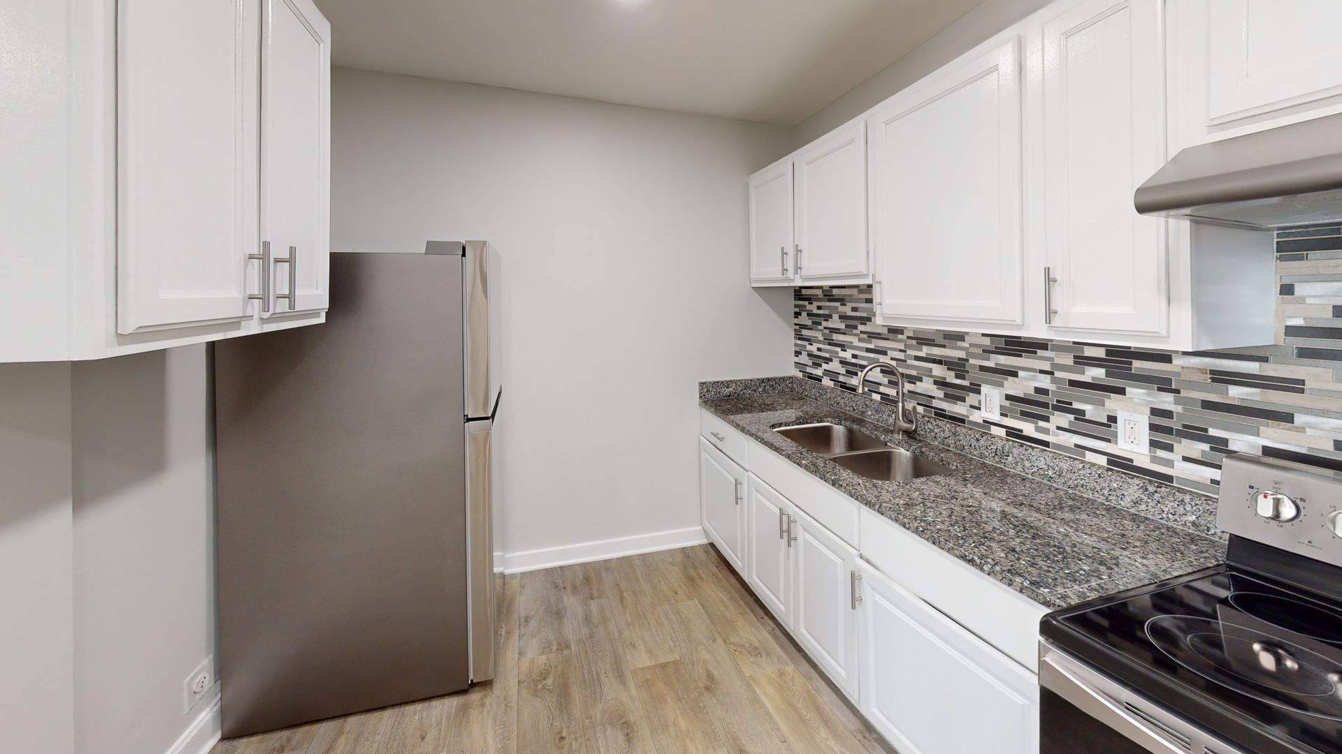 Modern kitchen with white cabinets, gray granite counters, stainless fridge, and mosaic backsplash