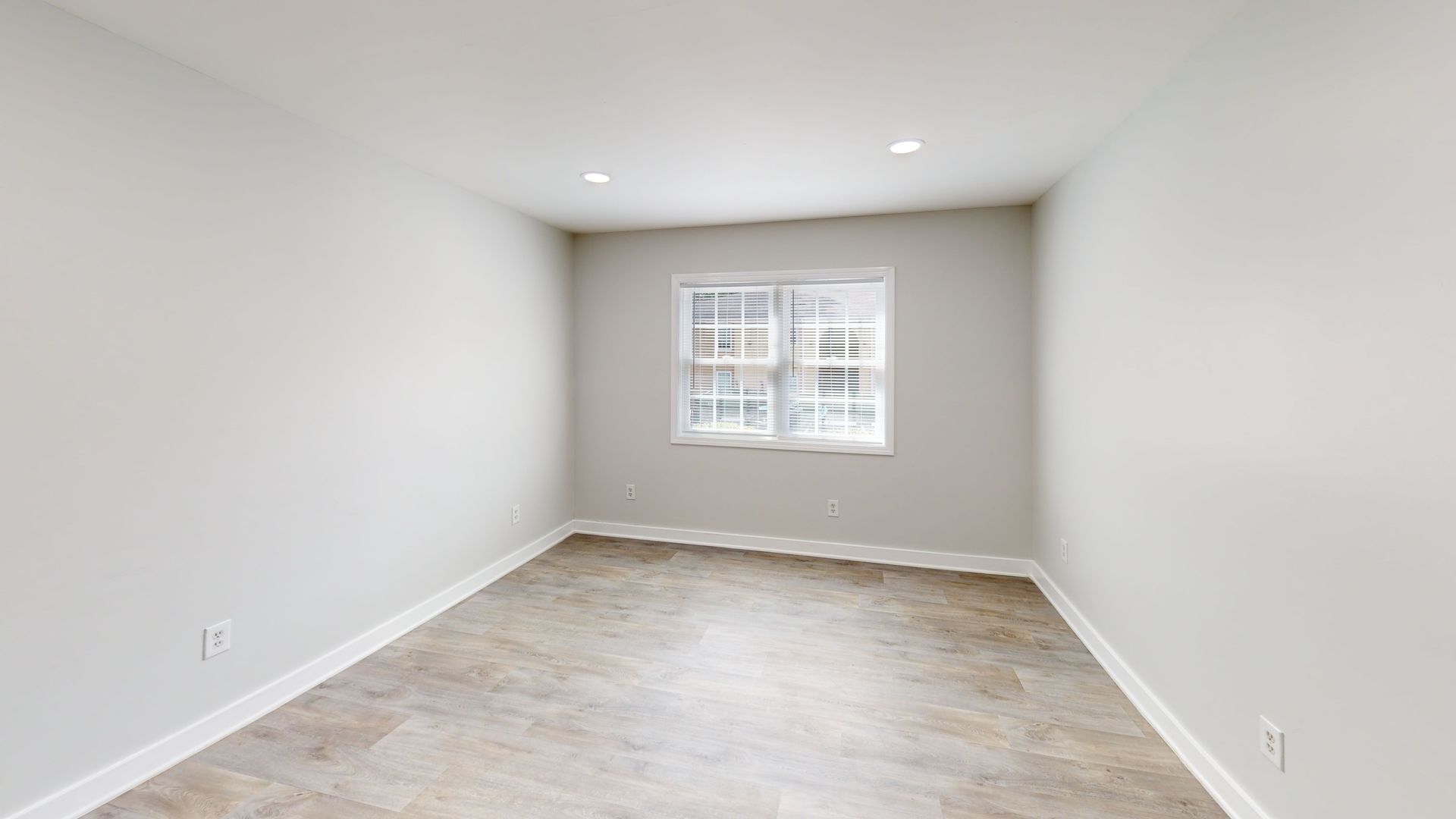 Empty white room with gray flooring and a small window at the far wall.
