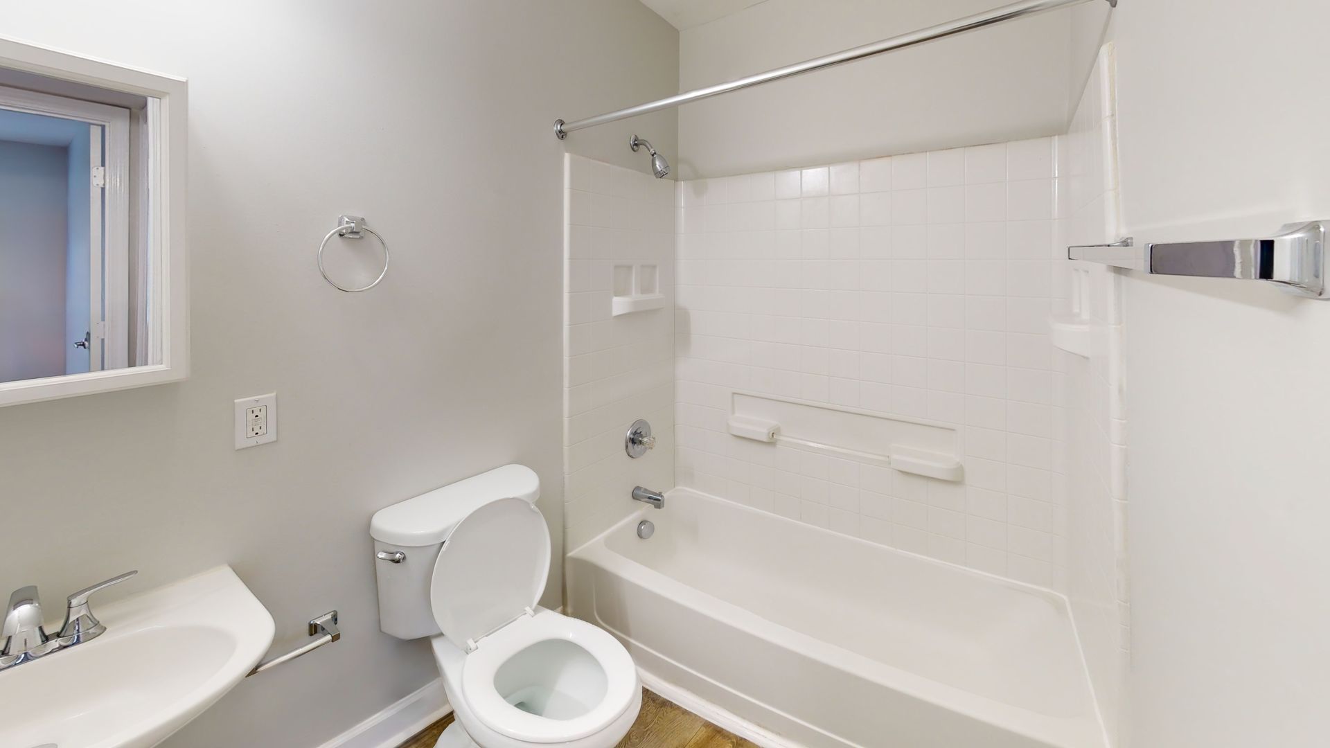 Bright bathroom with toilet, sink, and white bathtub-shower combo, viewed from the doorway.