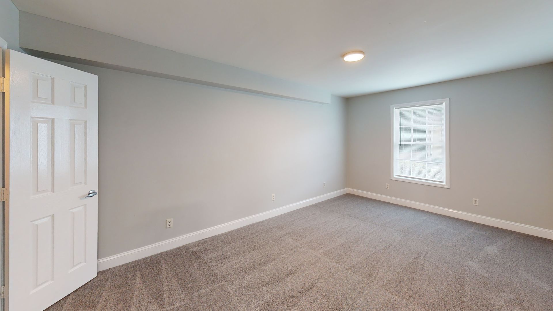 Empty carpeted bedroom with light gray walls, a window, and a closet door.