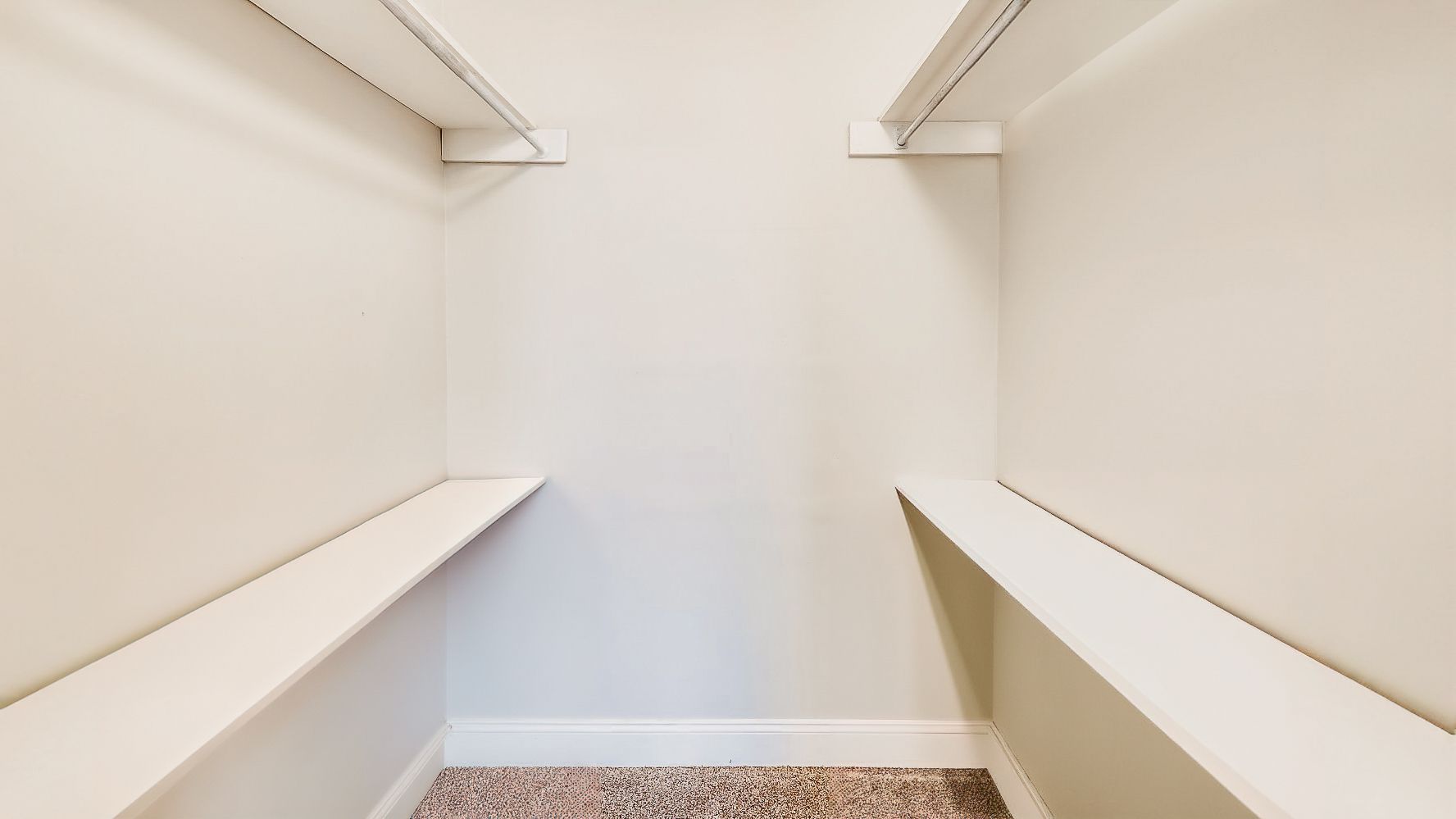 Empty white walk-in closet with built-in shelves and hanging rods