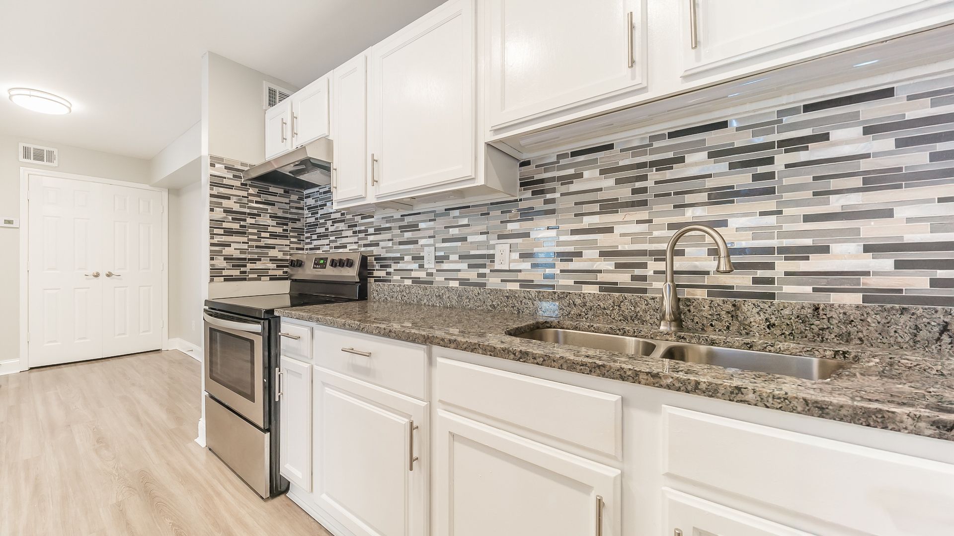 Bright white kitchen with stainless stove, granite counters, and gray mosaic tile backsplash