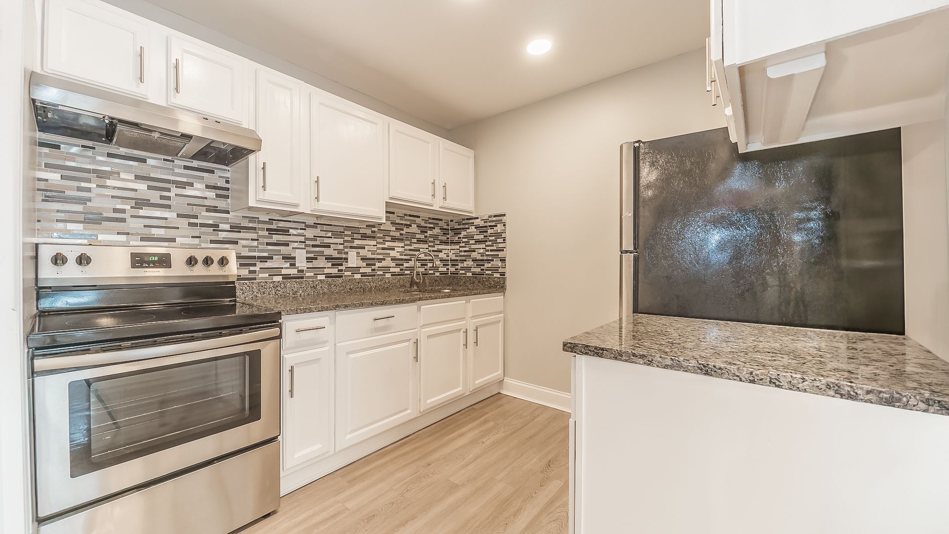 Modern kitchen with stainless steel appliances, white cabinets, mosaic backsplash, and granite counters