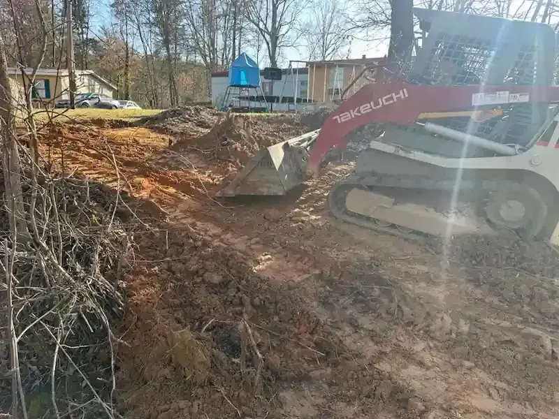 Red excavator clearing dirt on a wooded construction site near houses
