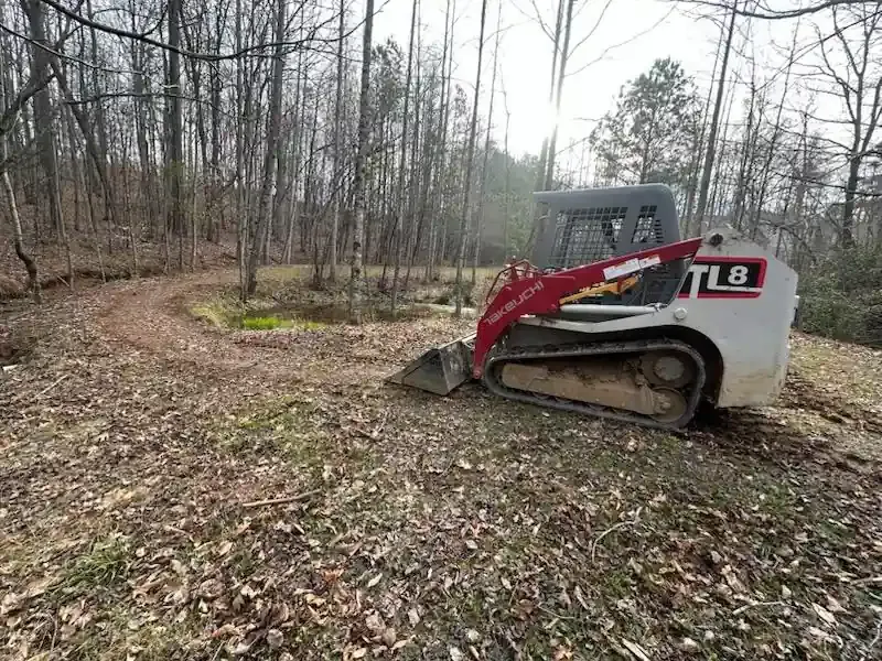 Red and white skid steer parked in a leaf-covered wooded clearing.