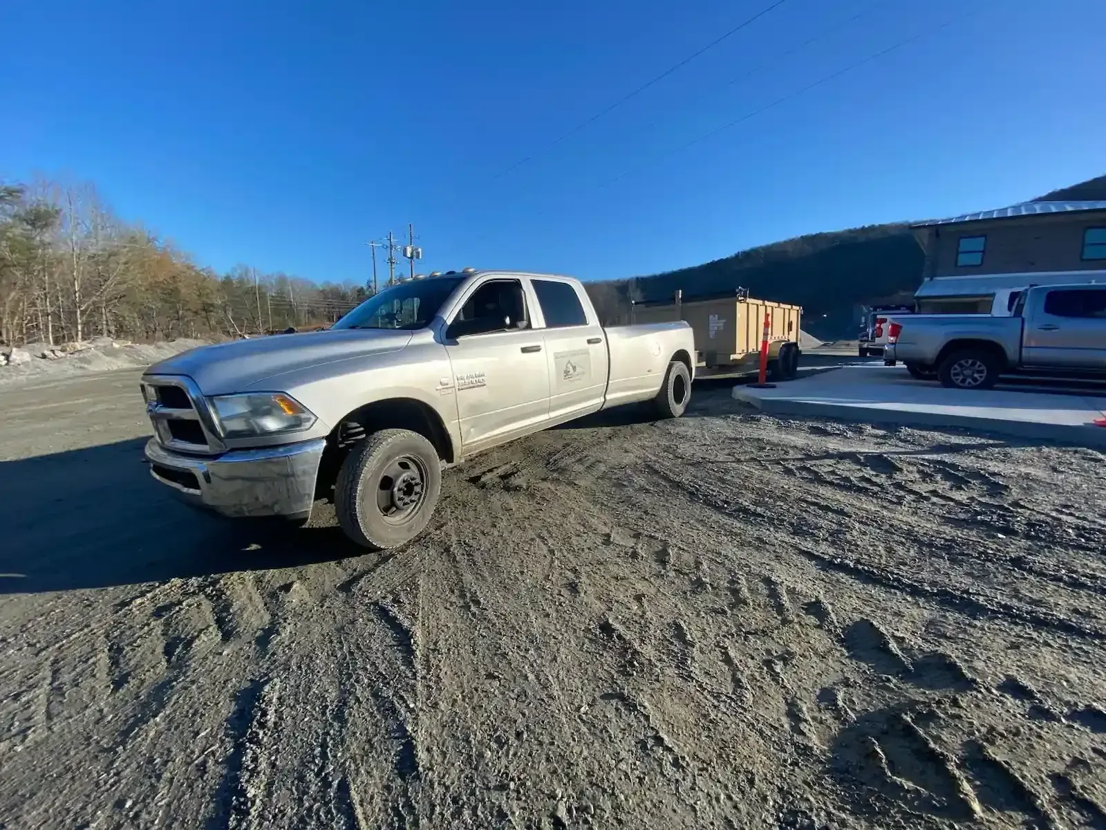 White pickup truck on a dirt lot with a trailer, beside a building under a clear blue sky