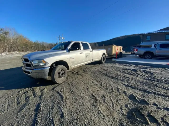 White pickup truck on a dirt lot with a trailer, beside a building under a clear blue sky