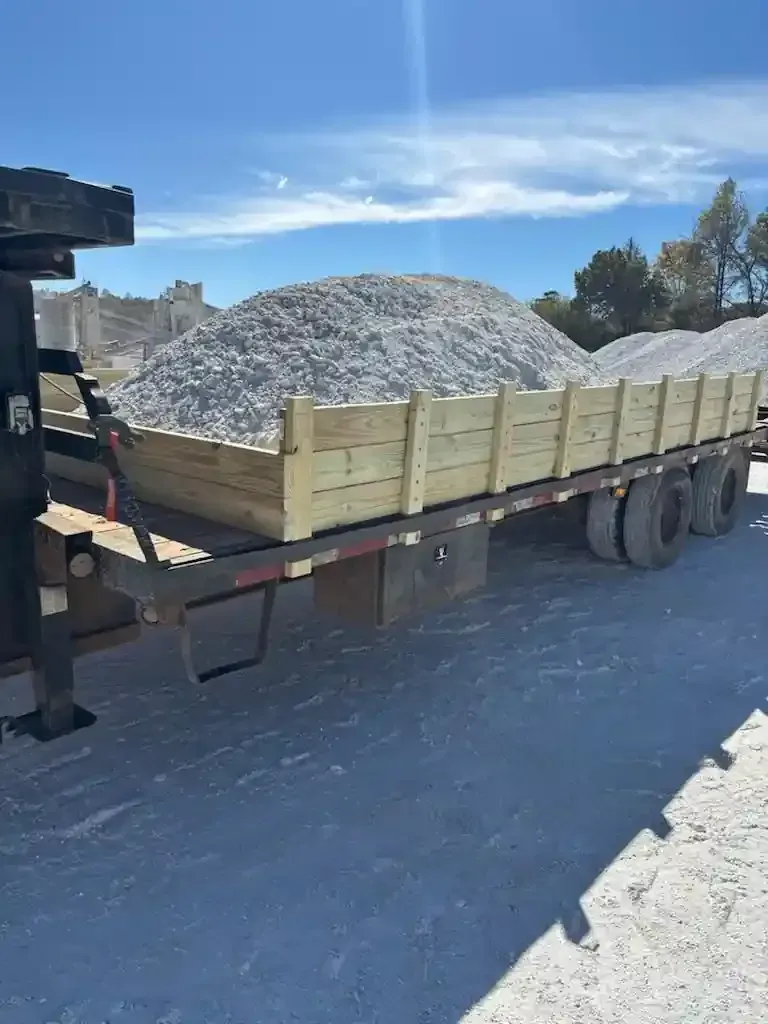 Flatbed trailer loaded with white gravel at a construction site under a blue sky