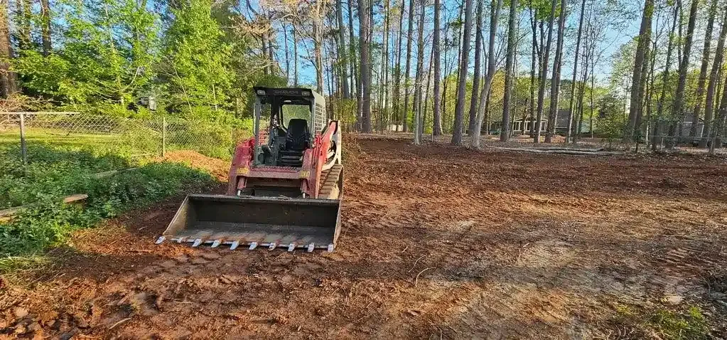 Bulldozer leveling a dirt field beside a line of trees