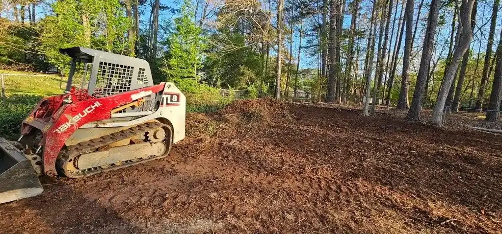 Red skid-steer clearing a leaf-covered wooded lot in autumn