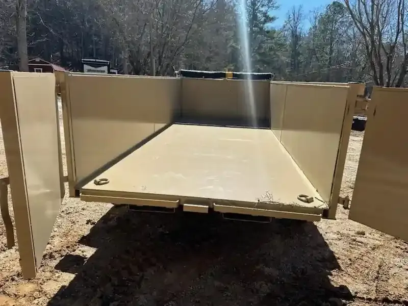 Open tan metal dump trailer with tailgate lowered over a dirt path