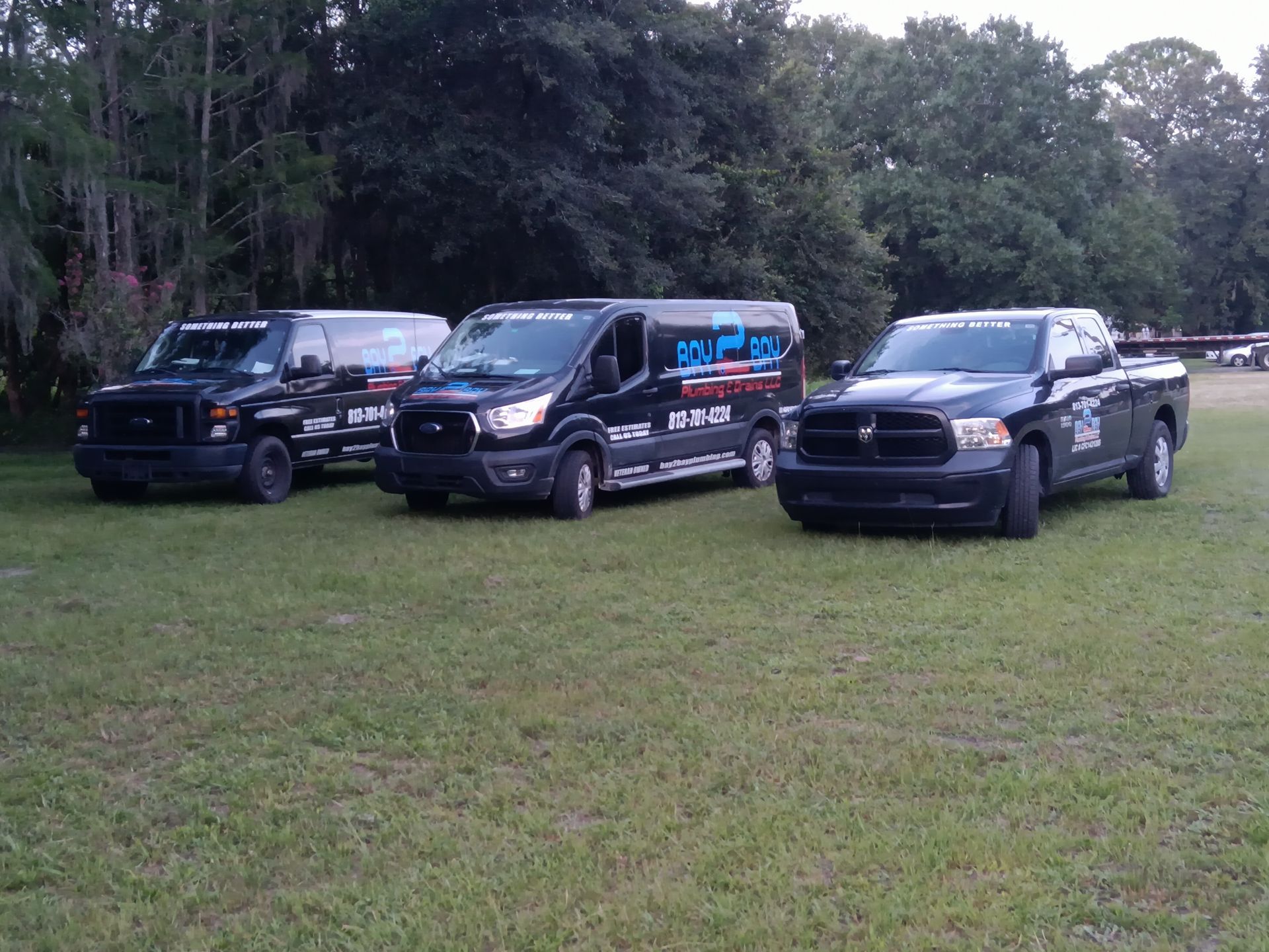 Three black pickup trucks parked on a grassy field with trees in the background.