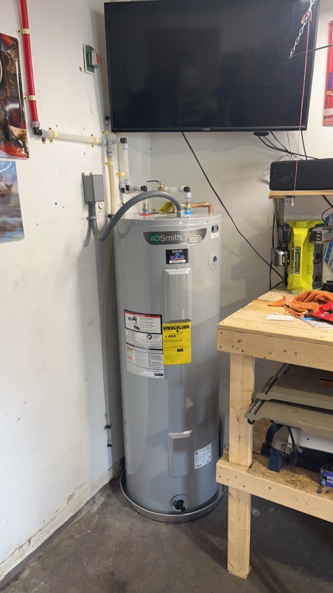 Water heater beneath a wall-mounted TV in a small utility area, beside a workbench and shelves