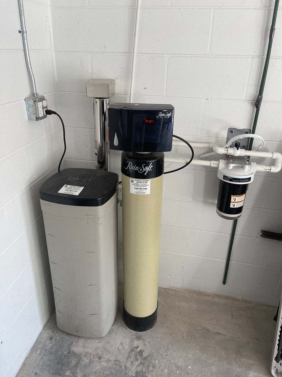 Water softener and filtration tanks installed against a white cinderblock wall.