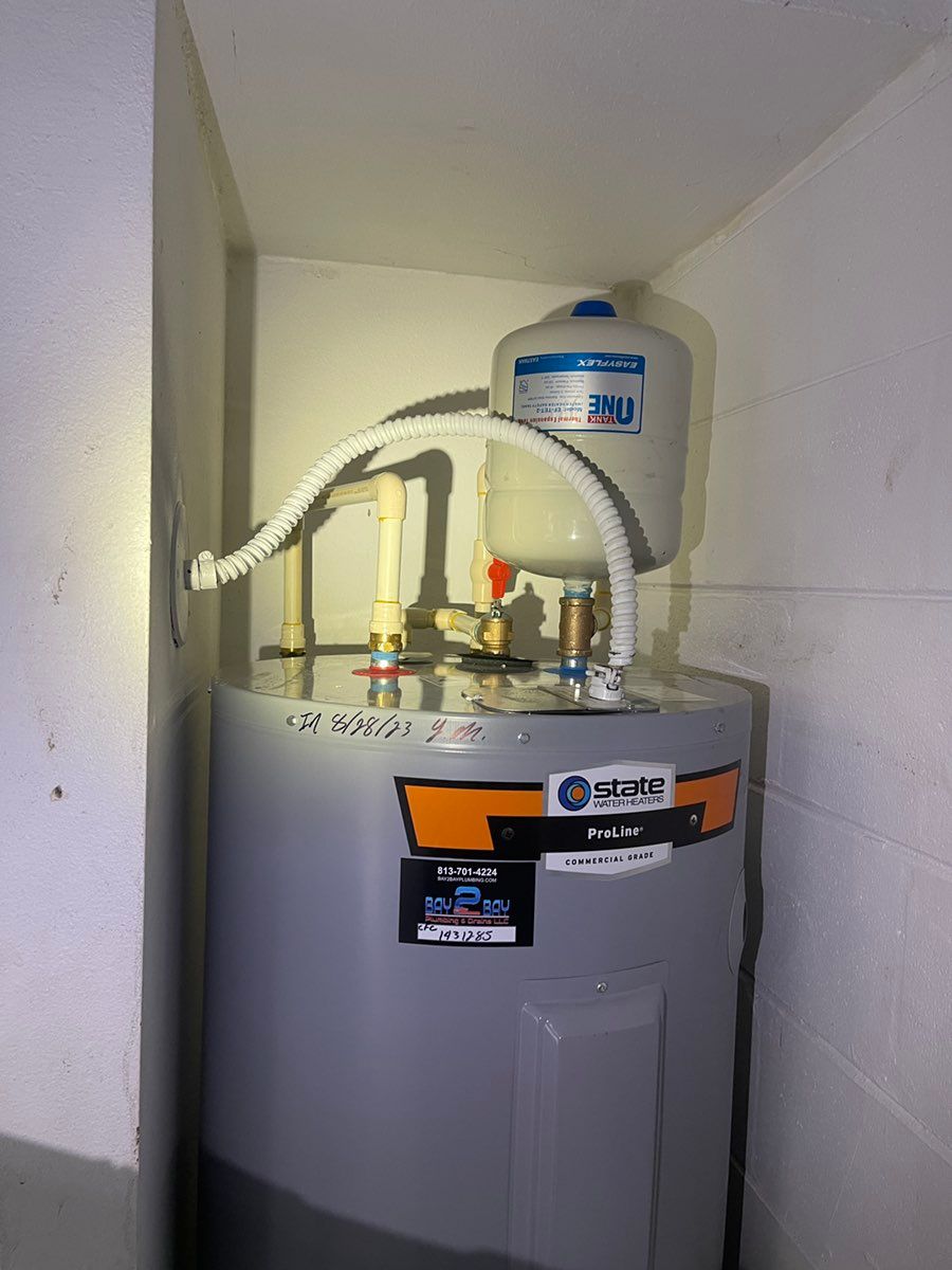 Water heater in a closet with white pipes and a small tank on top against beige walls.