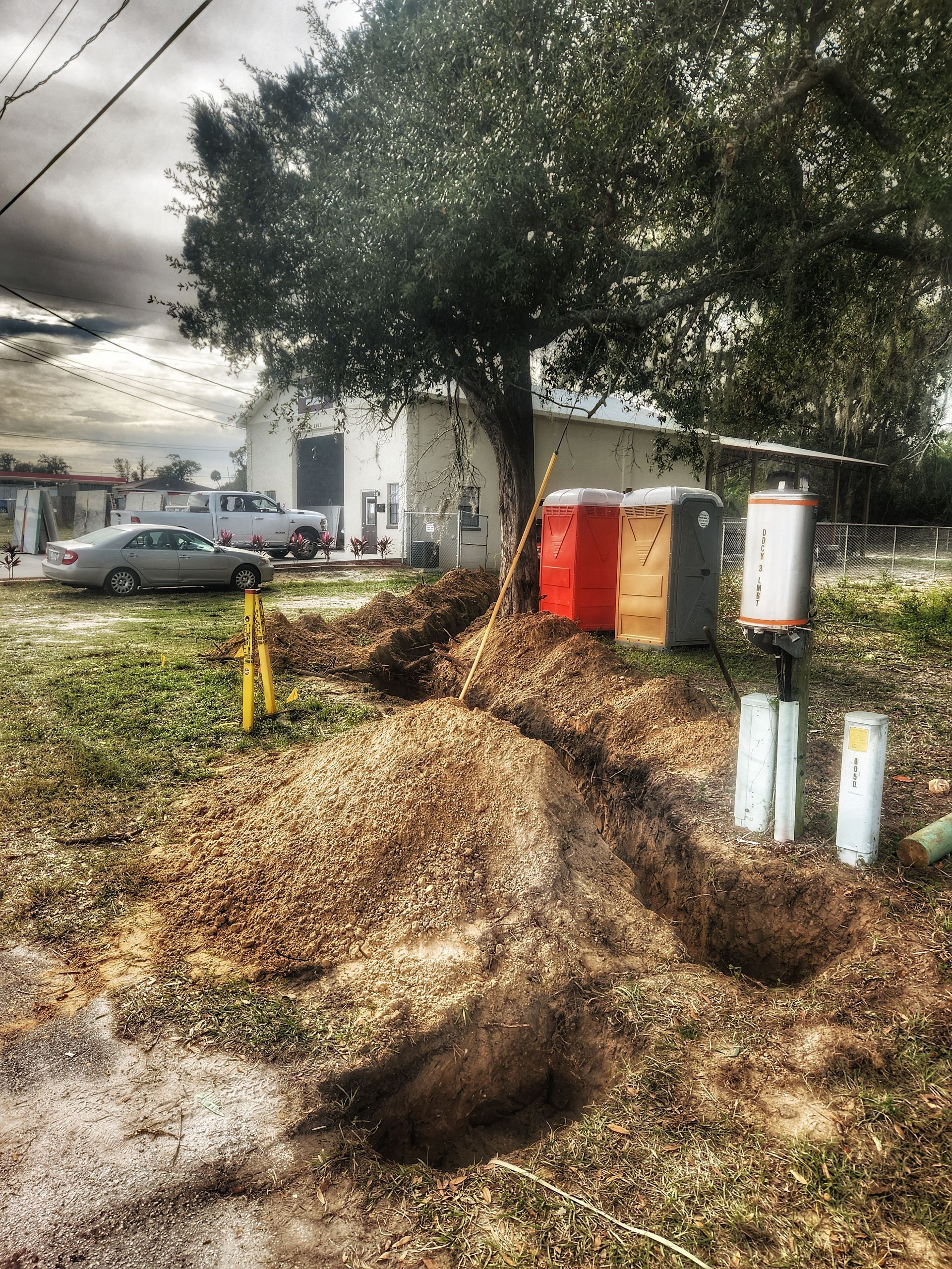 Utility boxes beside a large tree with uprooted soil and debris on a residential street