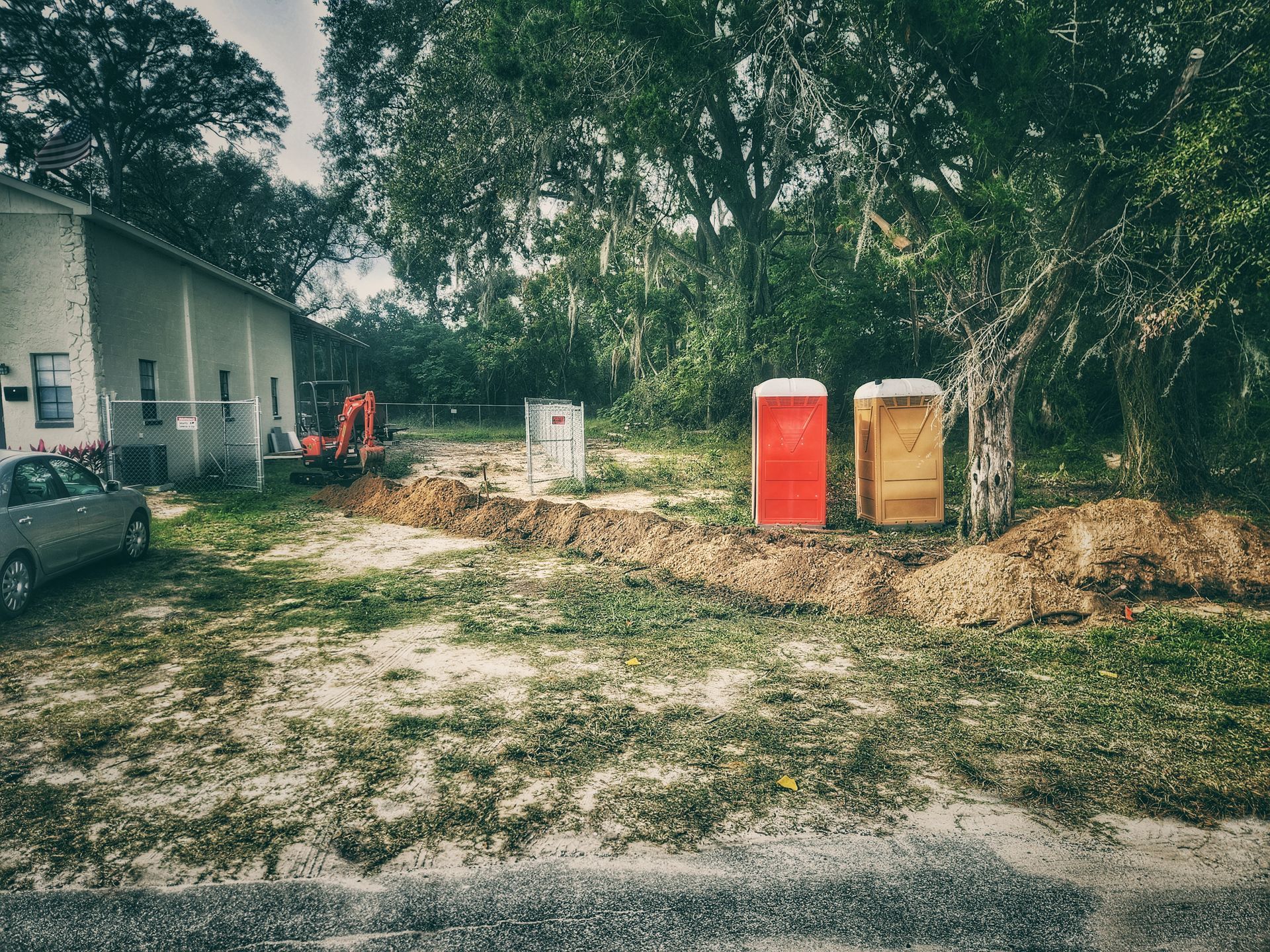 Rural yard with two portable toilets and a house near trees and dirt piles