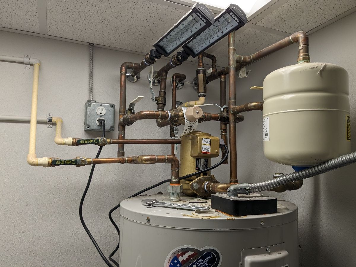 Residential boiler and plumbing setup with pipes, gauges, and a beige expansion tank in a utility room