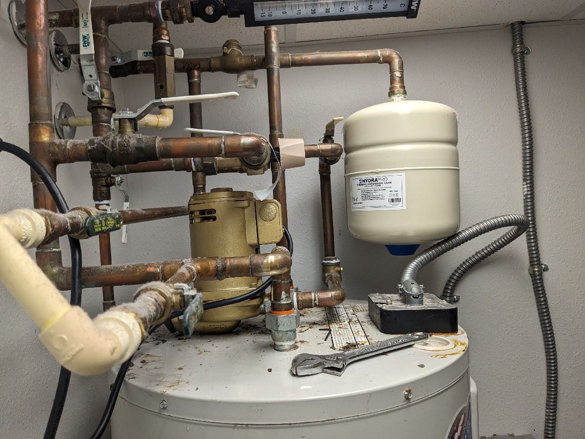 Heating equipment and piping in a utility room, with a white expansion tank and metal boiler unit.