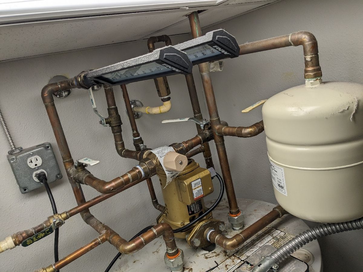 HVAC piping and boiler equipment with copper pipes, valves, and a large white expansion tank in a utility room