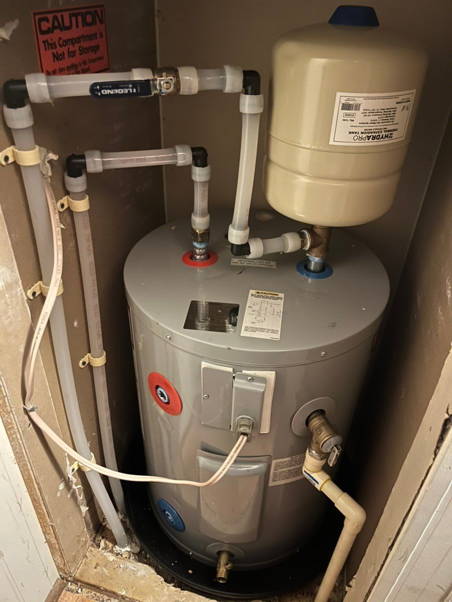 Water heater and plumbing in a utility closet, with a white expansion tank and exposed pipes.