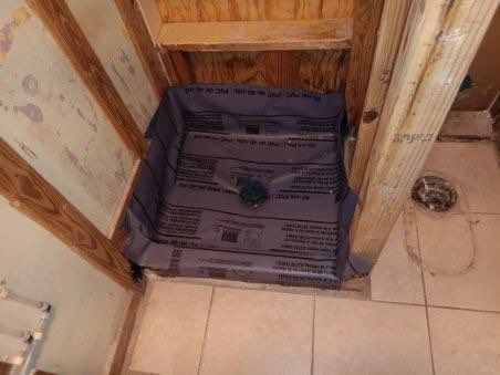 Bathroom shower floor with a dark waterproof liner installed in a corner stall