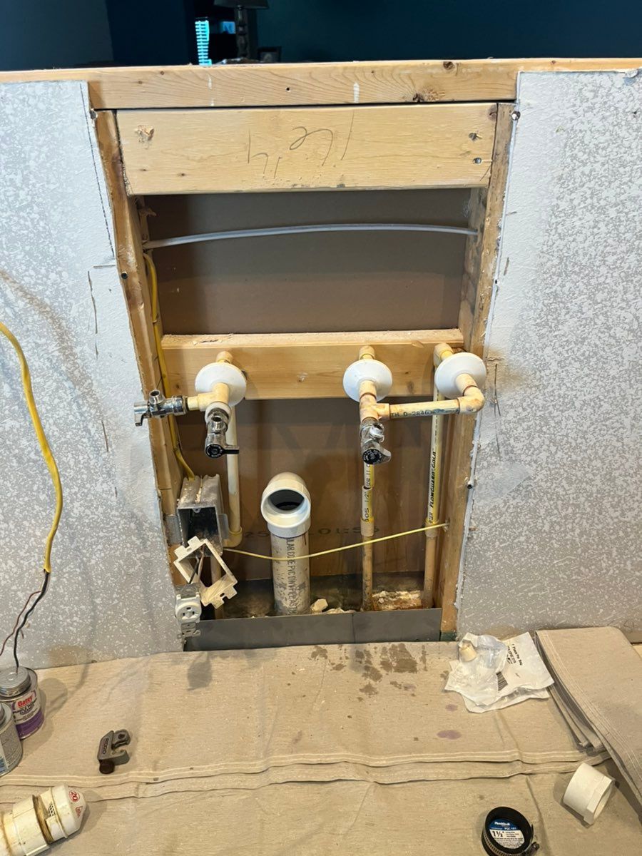 Open wall with exposed plumbing pipes and valves beneath a sink or shower area.