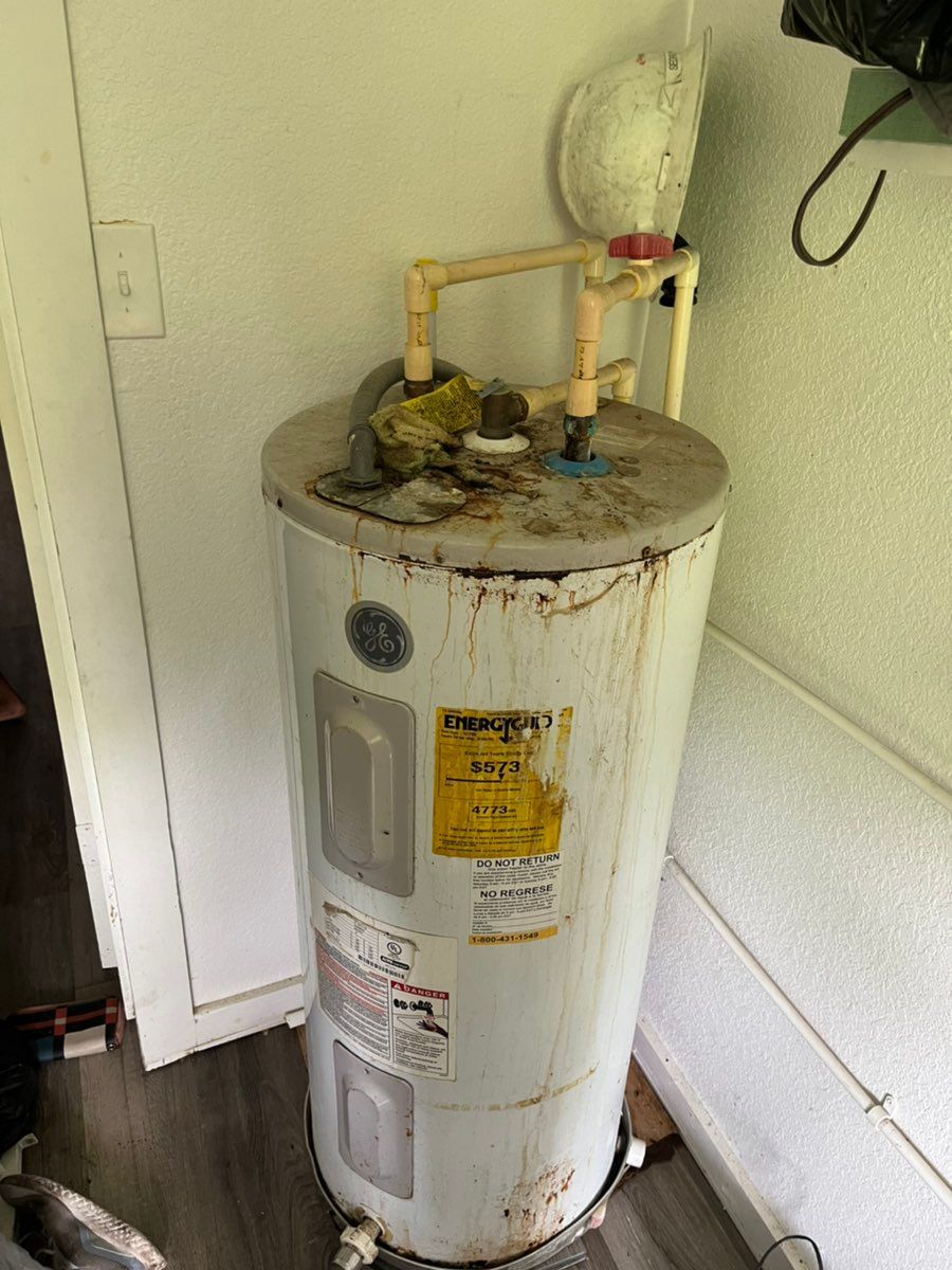 Old white water heater with rust and pipes in a utility closet