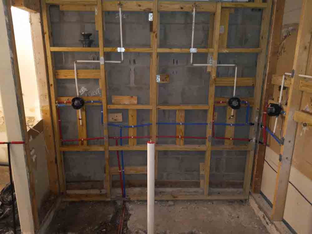 Partially framed shower wall with exposed plumbing and red/blue pipes in an unfinished bathroom