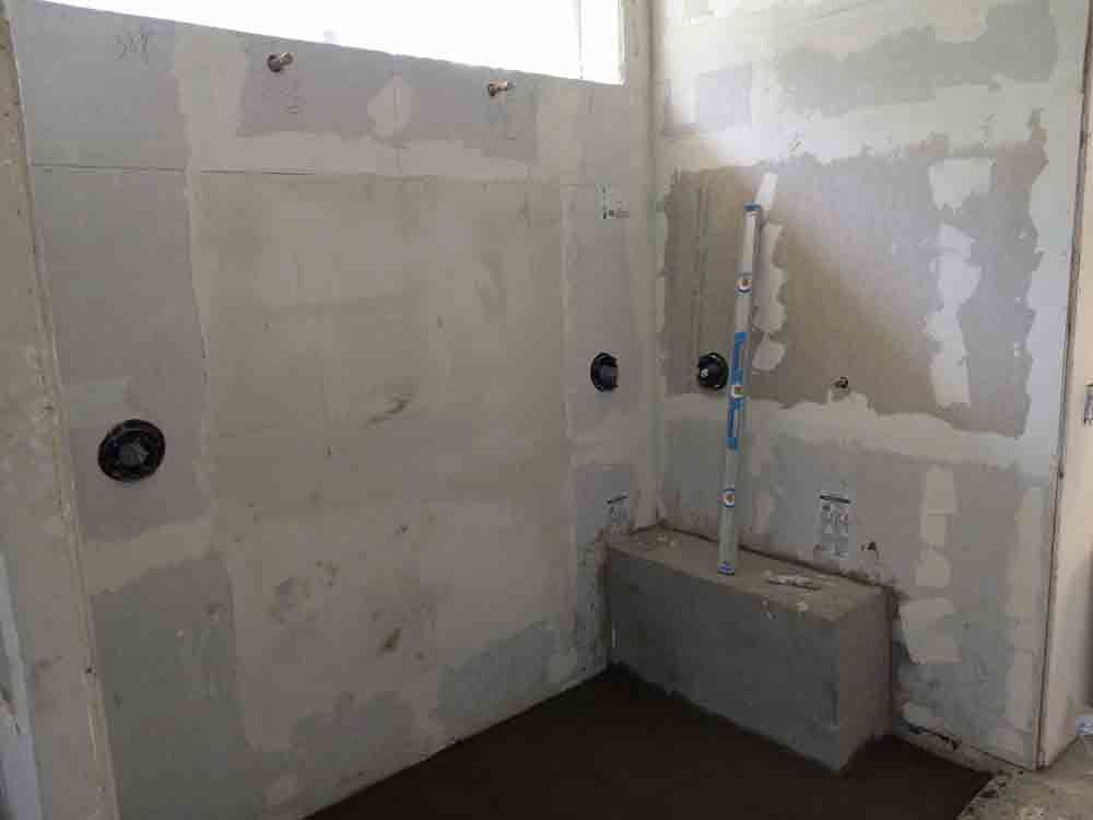 Unfinished bathroom with patched drywall, plumbing pipes, and a small wall-mounted sink basin.