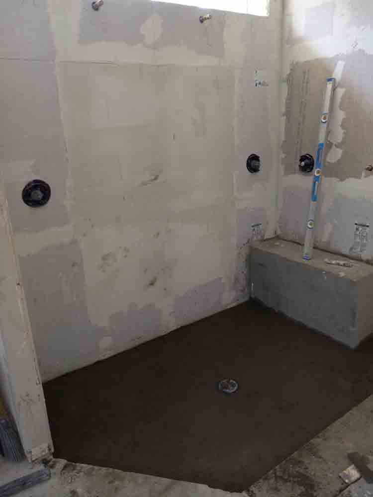 Partially finished bathroom with a shower area, exposed walls, and a dark floor base.