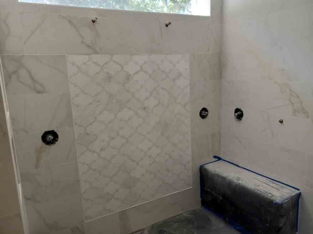 Partially tiled bathroom wall with electrical outlets and a black toolbox on the floor