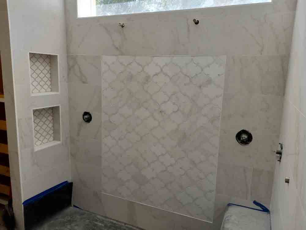 Empty white-tiled shower stall with built-in shelves and a glass-block window above.