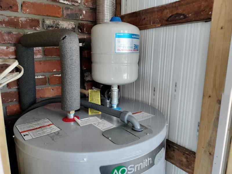 AO Smith water heater with expansion tank in a utility closet against brick and panel walls