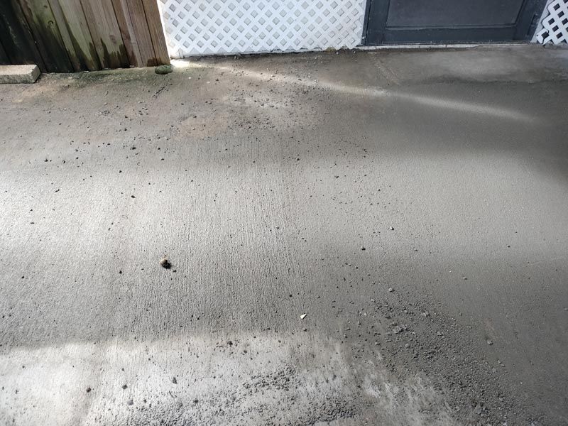 Shaded concrete driveway with scattered debris near a white gate and fence