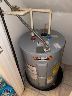 Water heater with pipes and valves in a small utility closet, gray tank on the floor.