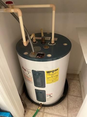 Water heater in a small utility closet with exposed pipes and warning labels.