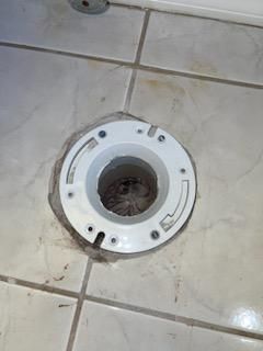 White toilet flange ring on tiled bathroom floor around an open drain hole