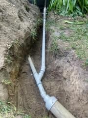 PVC pipes connected in a dirt trench, branching into two lines underground