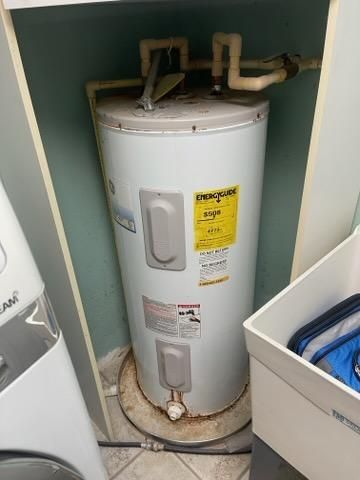 White water heater in a closet with exposed pipes and a yellow label.