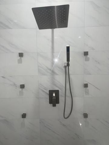 Modern shower with large square black rainfall head, handheld spray, and marble-look tiled wall