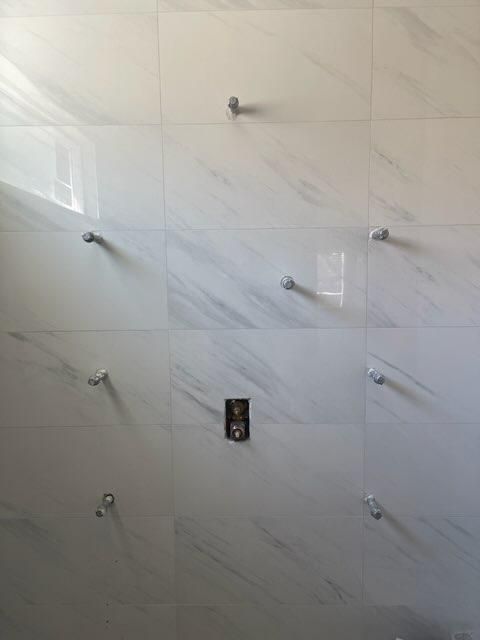 Tiled bathroom wall with multiple plumbing outlets and a central electrical box.