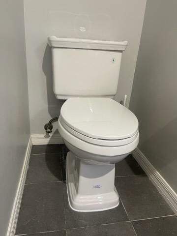 White toilet in a small gray-tiled bathroom corner
