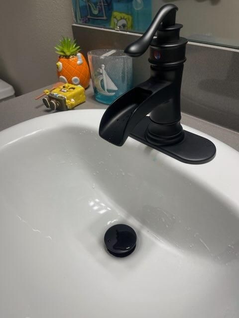 Bathroom sink with black faucet and drain, small toy car and plant on the counter behind it