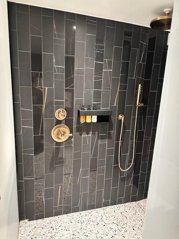 Dark tiled walk-in shower with black fixtures, built-in shelf, and pebble-pattern floor.