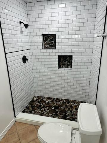 Small tiled shower with black fixtures, two recessed niches, and pebble floor beside a toilet.