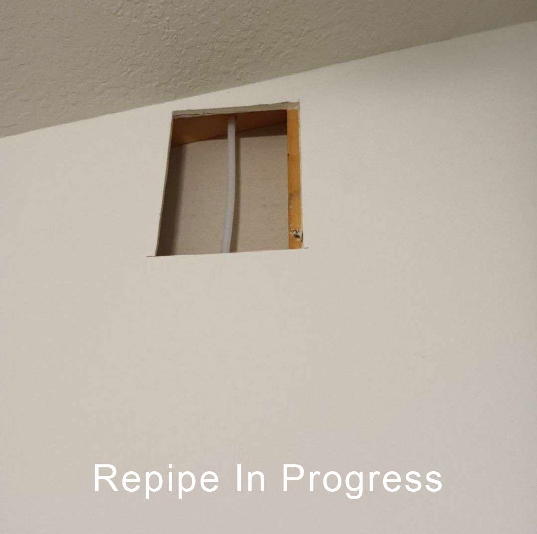 Wall with a square cutout exposing pipes during repiping work